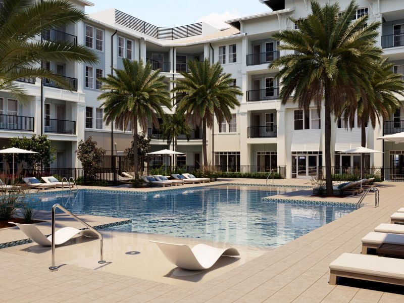 Modern apartment complex with palm trees, lounge chairs, and a swimming pool under a sunny sky.