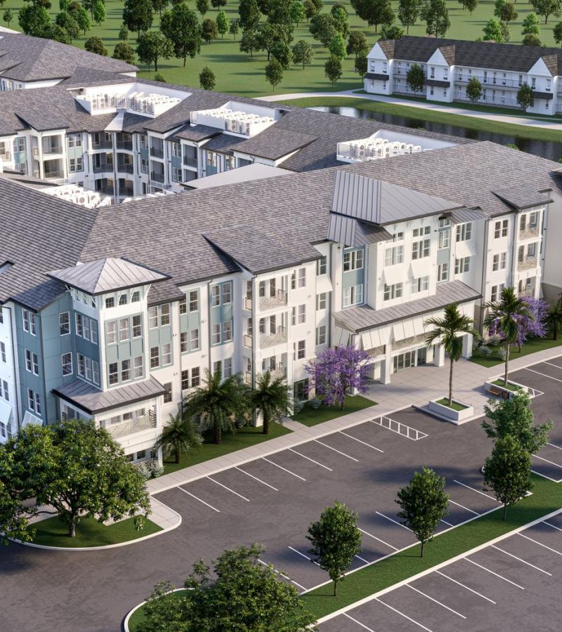 Aerial view of a large modern apartment complex with parking spaces and surrounded by trees.