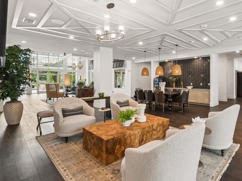 Modern lobby with cozy seating, wooden coffee table, pendant lights, plants, and large windows letting in natural light.